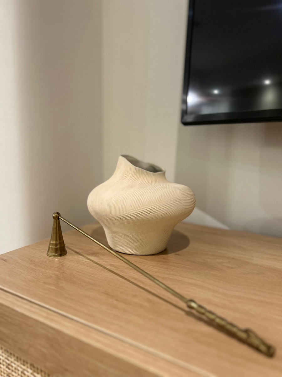 Styling detail: a sculptural ceramic vase and brass candle snuffer on an oak sideboard