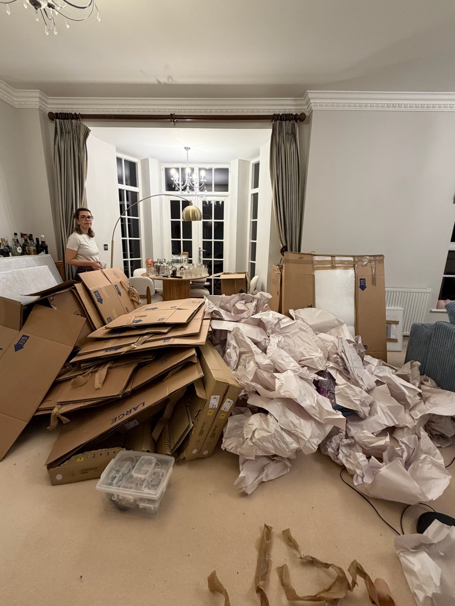 Unpacking under way in the dining room of the Sevenoaks home, with flattened boxes and packing paper piled across the floor and a person standing at the far end of the room